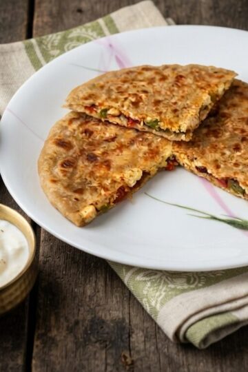Paneer capsicum paratha with onion stuffing served with curd, pickle, and green chutney