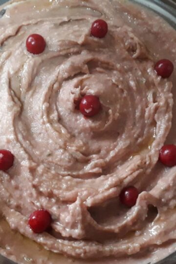 Creamy beetroot hummus topped with olive oil, parsley, and sesame seeds, served with pita bread and fresh vegetable sticks.