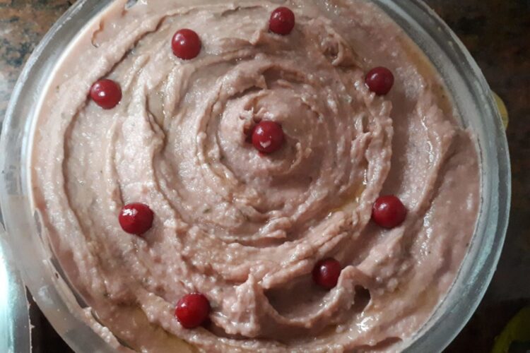 Creamy beetroot hummus topped with olive oil, parsley, and sesame seeds, served with pita bread and fresh vegetable sticks.