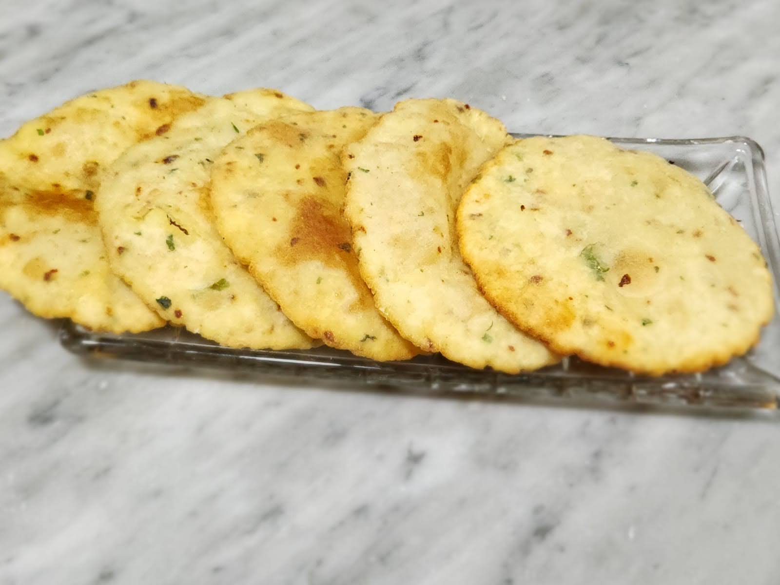 "A plate of crispy gluten-free Upvas Bhajni Aloo Pooris, golden brown and puffed, garnished with fresh coriander and served with a bowl of yogurt and green chutney, perfect for fasting days.